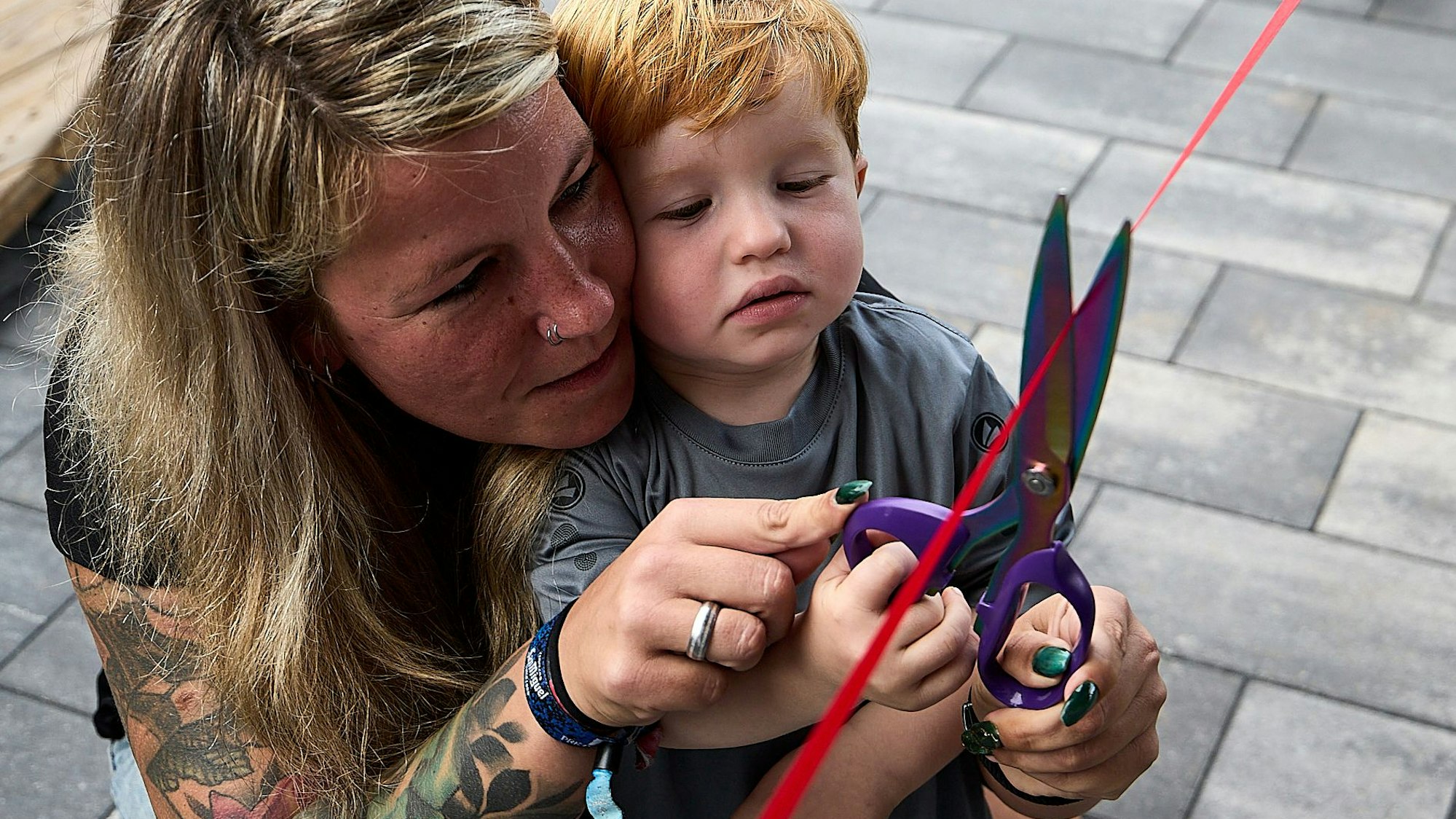 Konzentriert durchschneidet der kleine Junge das rote Band, eine Frau hilft ihm dabei.
