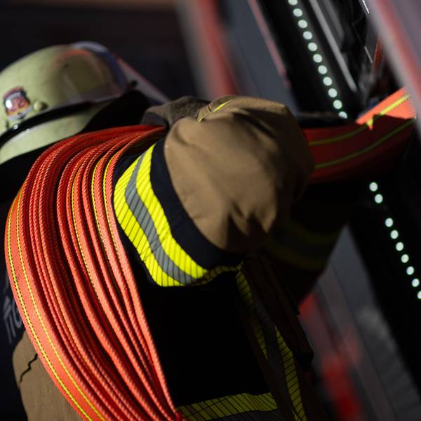 Eine Einsatzkraft der Feuerwehr nimmt einen Schlauch aus einem Einsatzfahrzeug. (Symbolbild)