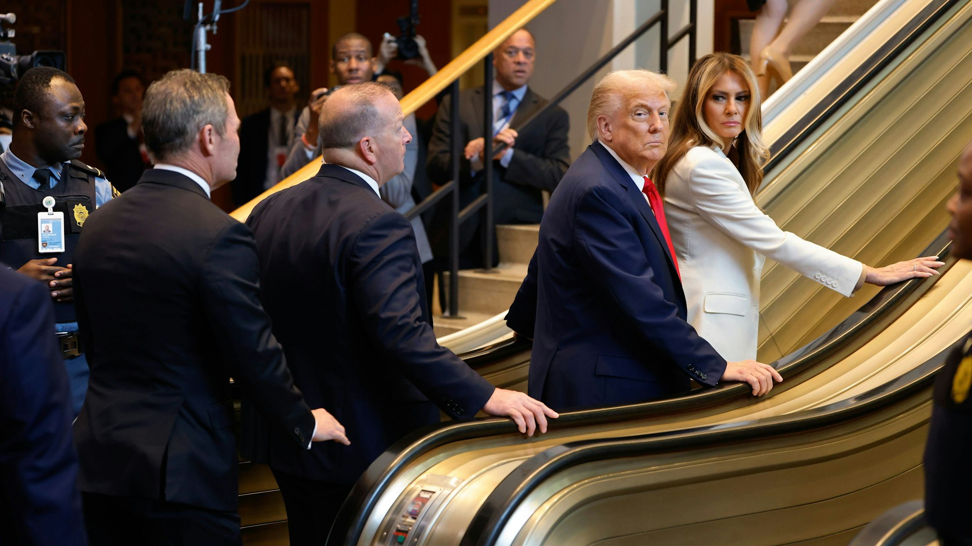 US-Präsident Donald Trump und First Lady Melania Trump schauen sich irritiert um, nachdem die Rolltreppe plötzlich stehen bleibt.