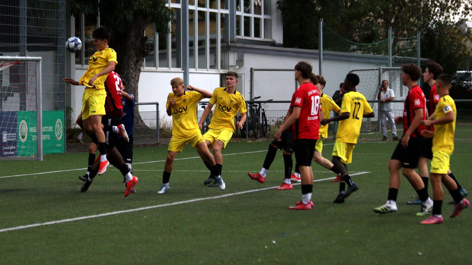 Ein Aachener Fußballer erreicht den Ball vor dem Gegenspieler der JSG Erft und dem gegnerischen Torwart per Kopf und erzielt ein Tor.