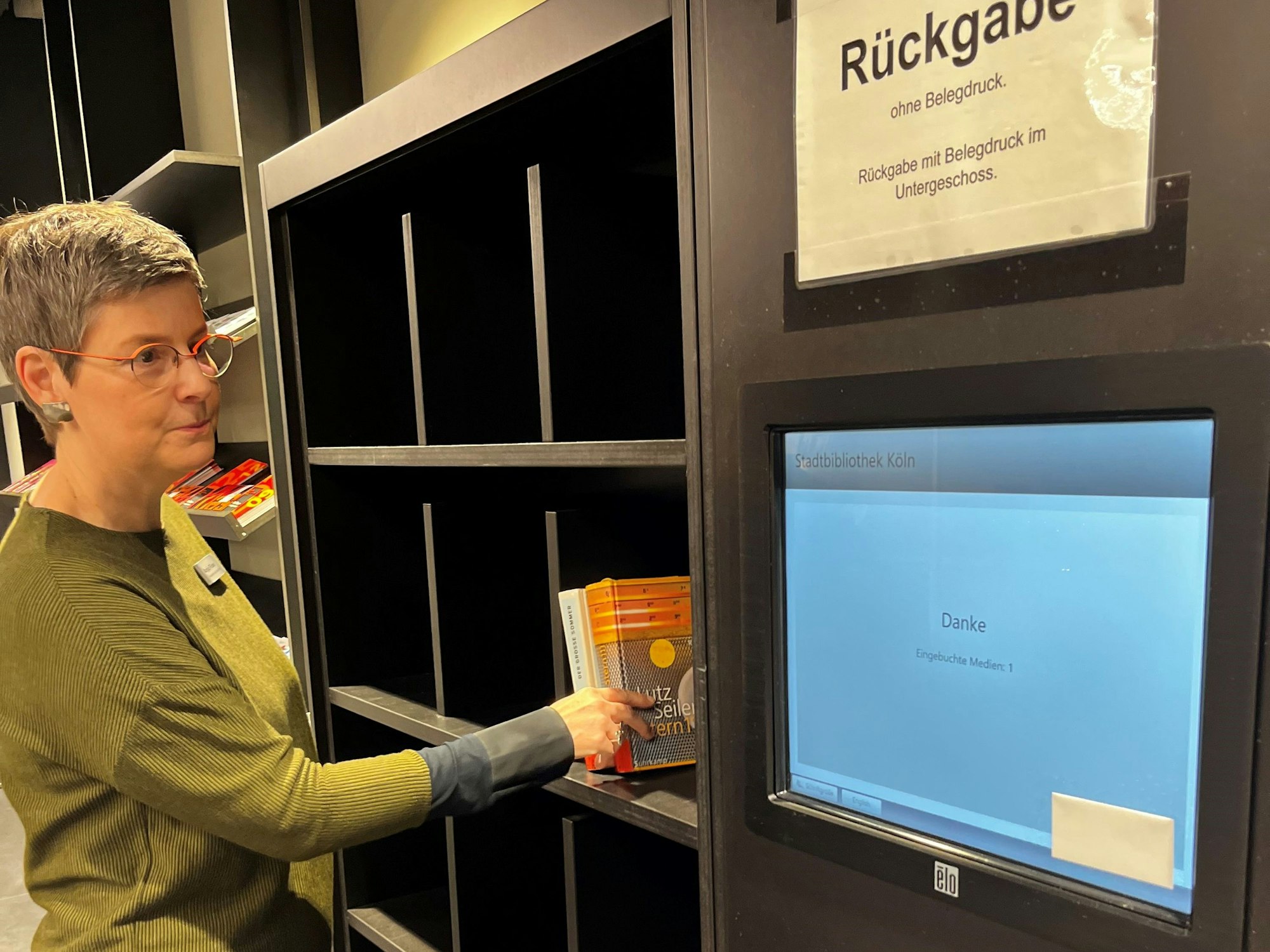 Direktorin Anja Flicker stellt ein Buch in das neue Regal für Rückgaben in Sekundenschnelle.