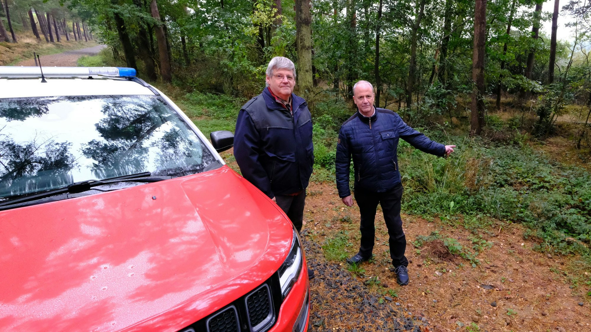 Ordnungsamtsleiter Harald Heinen (l.) und Bürgermeister Hermann-Josef Esser stehen in einem Waldgebiet in der Nähe von Kall neben einem Feuerwehr-Jeep.