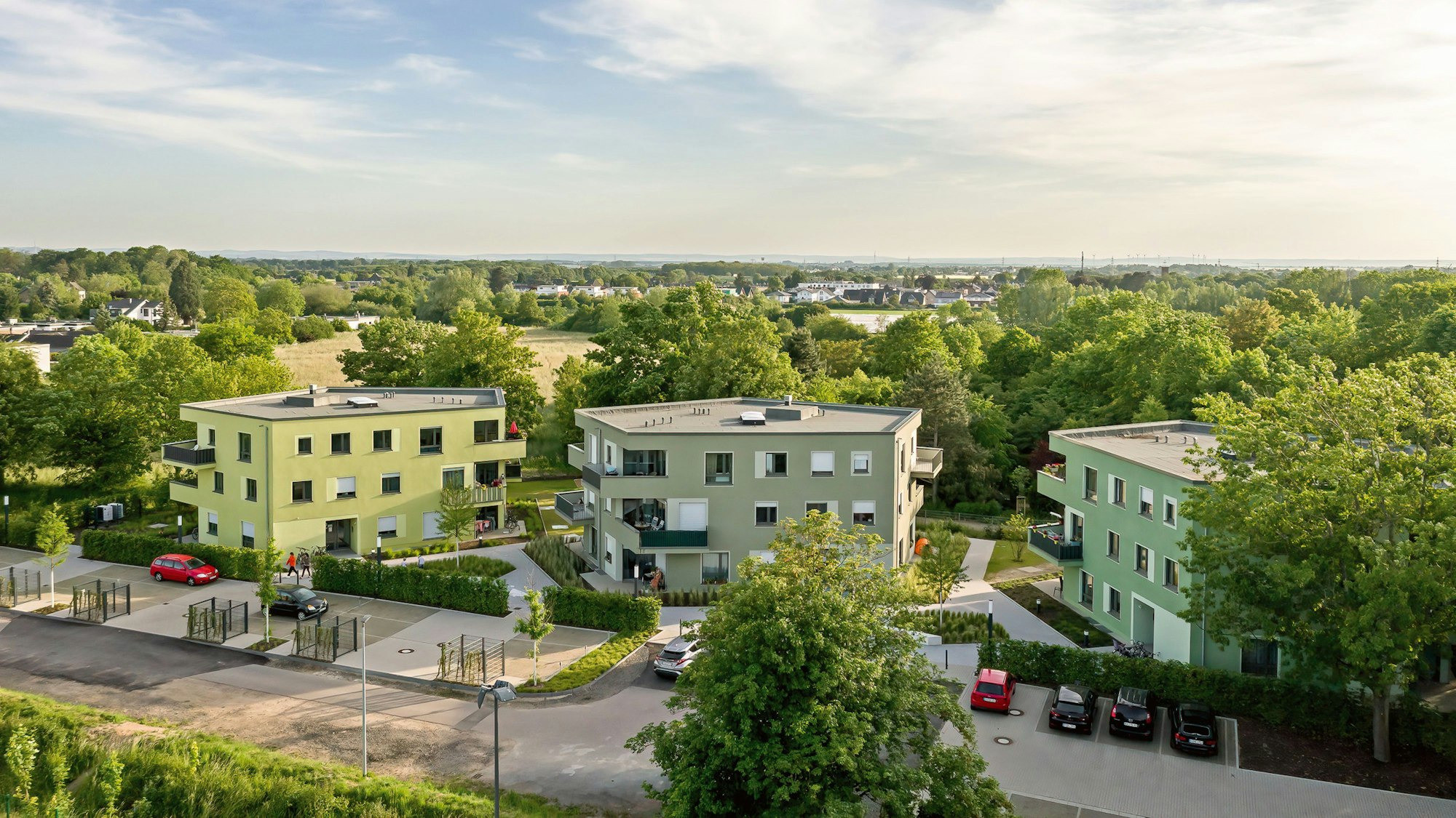 Zu sehen sind drei fünfeckige Häuser in einer grünen Umgebung.