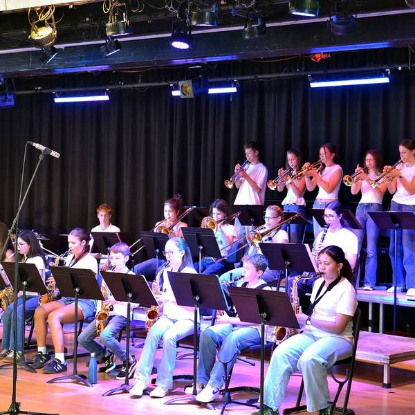 Ein Orchester mit jungen Musikern sitzt auf der Bühne, links agiert der Dirigent.
