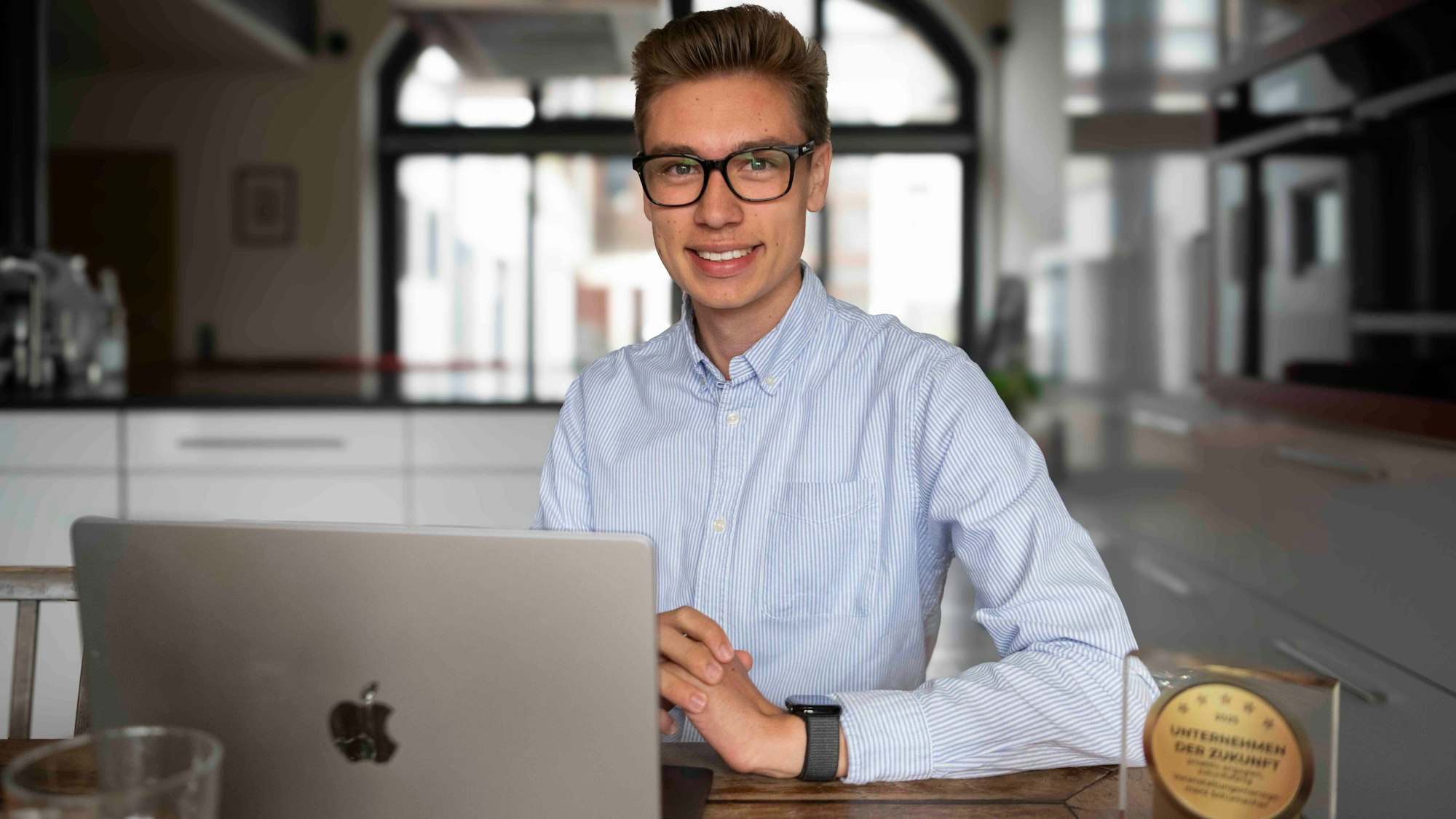 Das Bild zeigt David Schumacher am Küchentisch. Vor ihm steht ein Laptop und der gewonnene Preis.