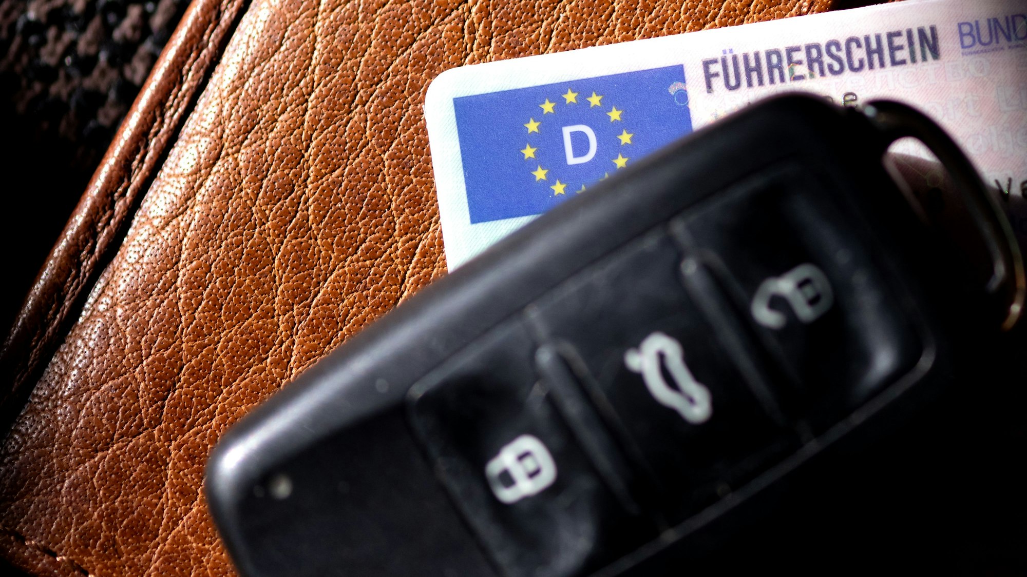 Ein Führerschein und ein Autoschlüssel liegen auf einem Portemonnaie.