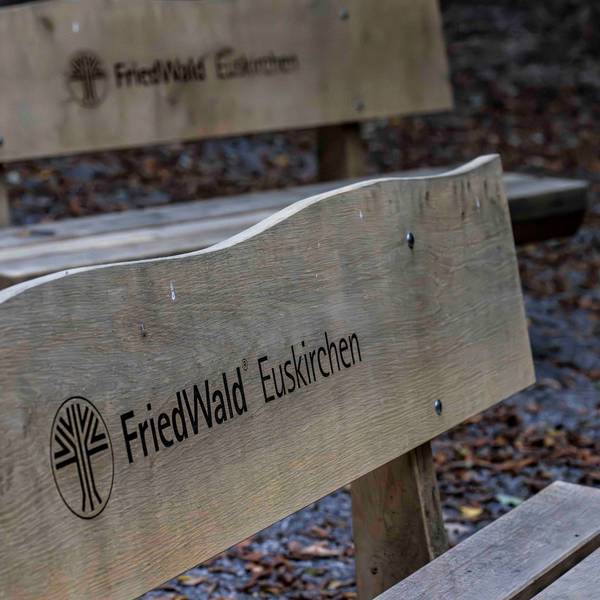 Das Bild zeigt zwei Holzbänke für Trauergäste. Sie tragen die Inschrift: Friedwald Euskirchen.