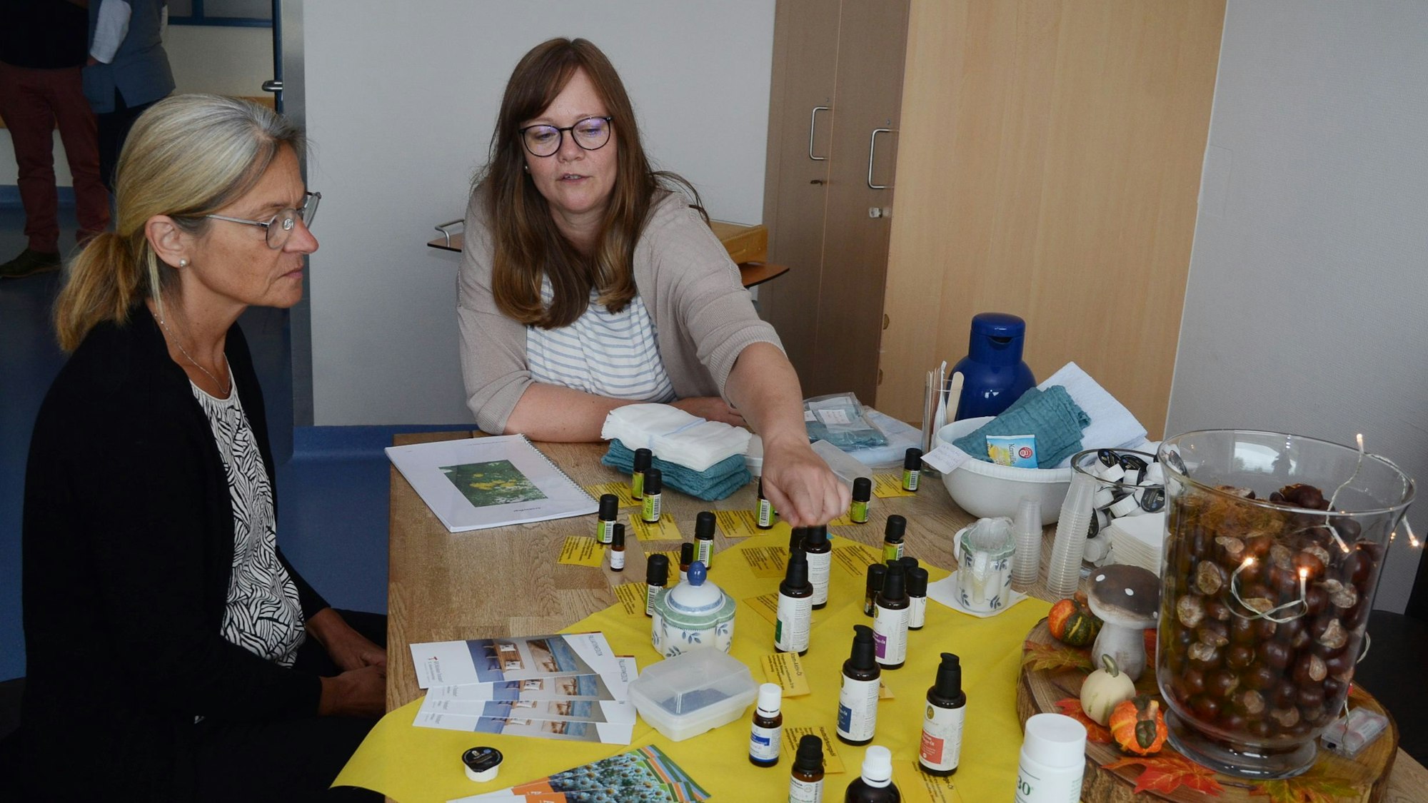 Zwei Frauen sitzen an einem Tisch, auf dem kleine Flakons mit Duftölen stehen.
