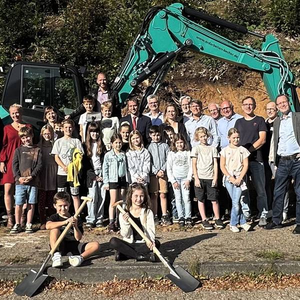 Vor einem Bagger stehen Bürgermeister Christoph Nicodemus sowie Schülerinnen und Schüler der Gemeinschaftsgrundschule Overath.