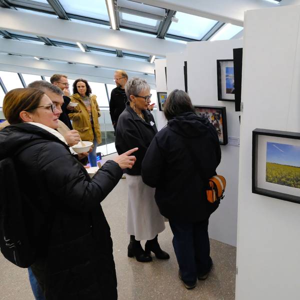 Eine Gruppe von Menschen steht vor einer Ausstellungswand, auf der mehrere gerahmte Bilder hängen.