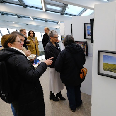 Eine Gruppe von Menschen steht vor einer Ausstellungswand, auf der mehrere gerahmte Bilder hängen.