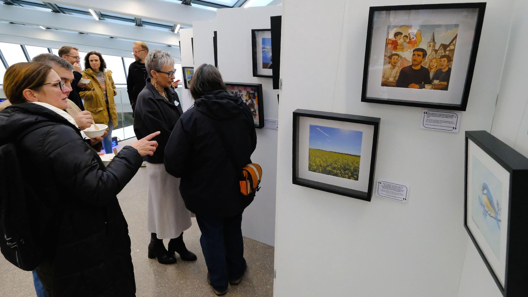 Eine Gruppe von Menschen steht vor einer Ausstellungswand, auf der mehrere gerahmte Bilder hängen.