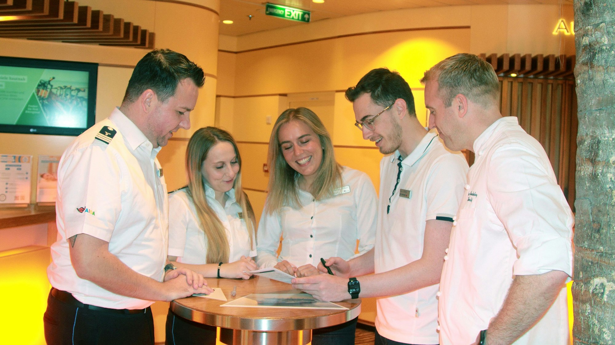 Die Genannten besprechen sich an einem Tisch an der Rezeption des Schiffs.