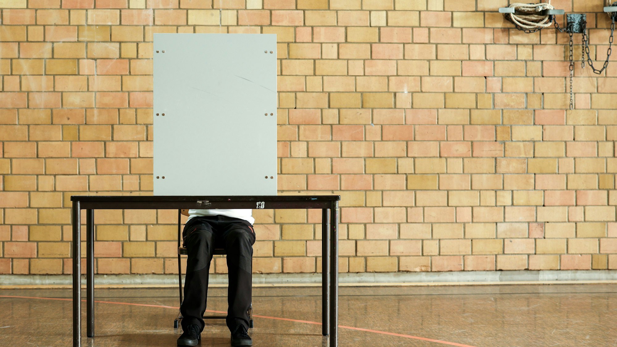 Ein Mann sitzt hinter einer Wahlkabine in einer Turnhalle.