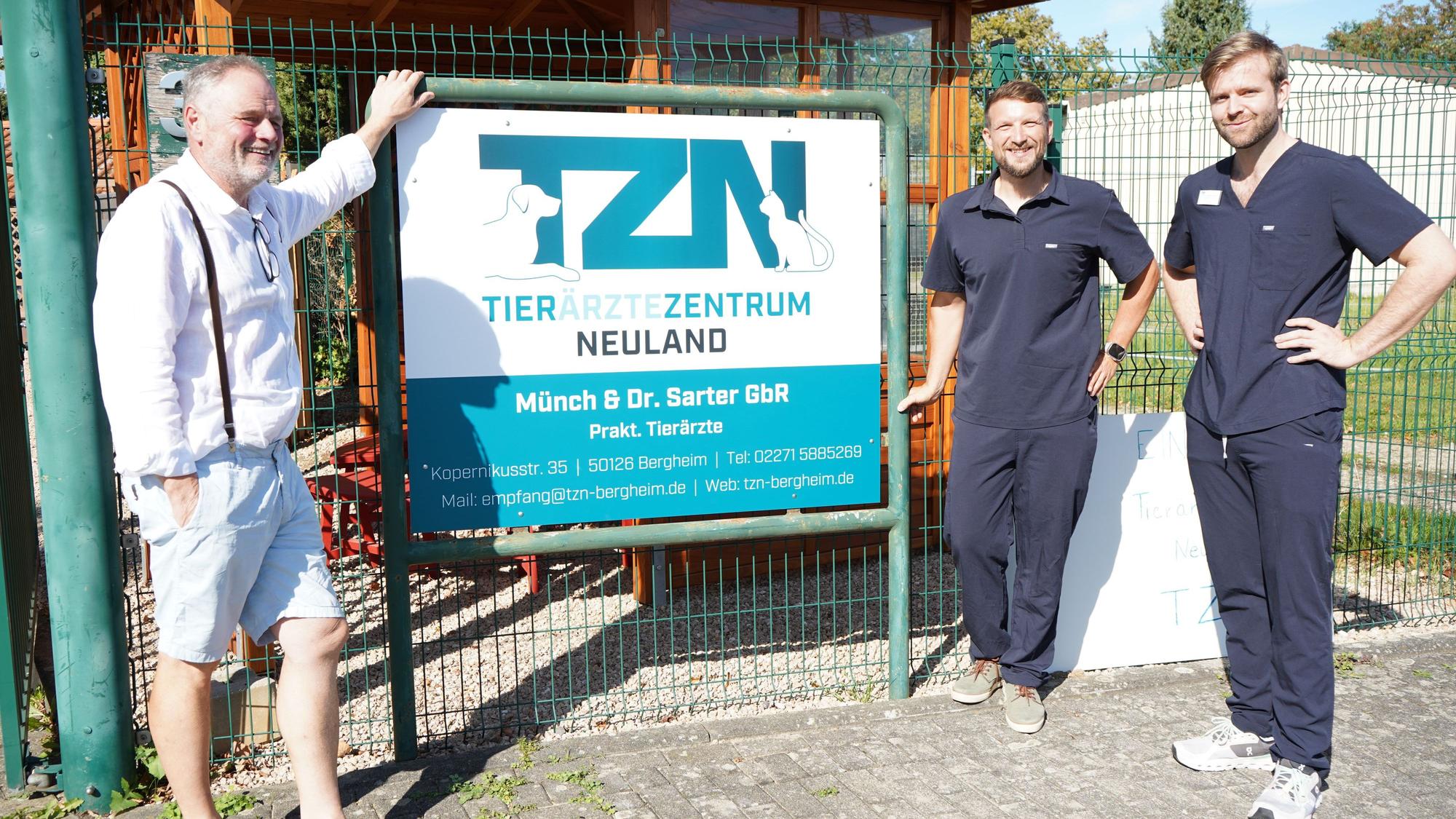 Das Foto zeigt drei Männer vor einem Schild.