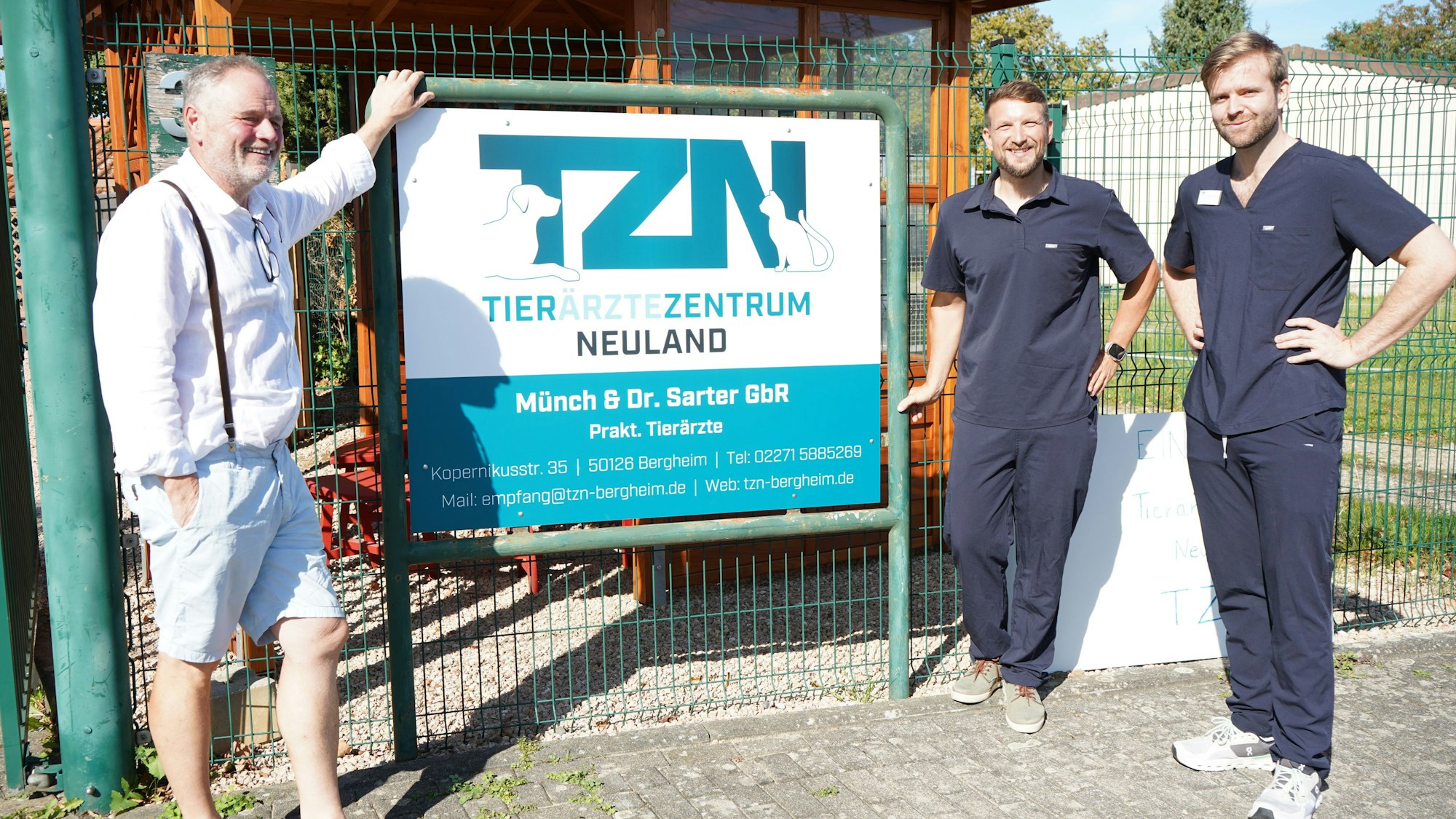 Das Foto zeigt drei Männer vor einem Schild.