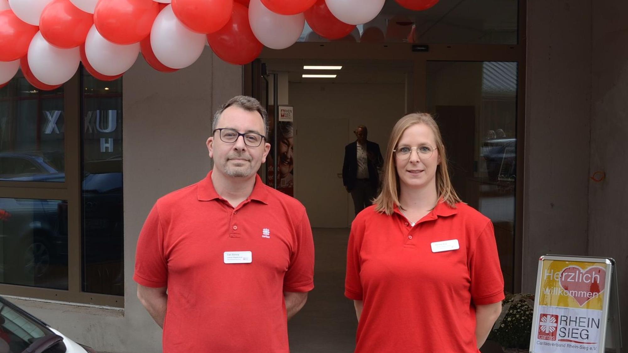 Ein Mann und eine Frau in roten Polohemden; über ihnen hängen rote und weiße Luftballons.