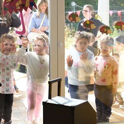 Vier Kinder blicken durch die Fensterscheibe.