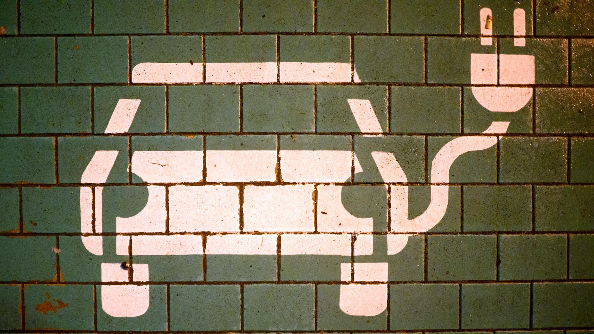 Ein Symbol markiert einen Parkplatz mit einer öffentlichen Ladesäule für Elektroautos an einem Einkaufszentrum.