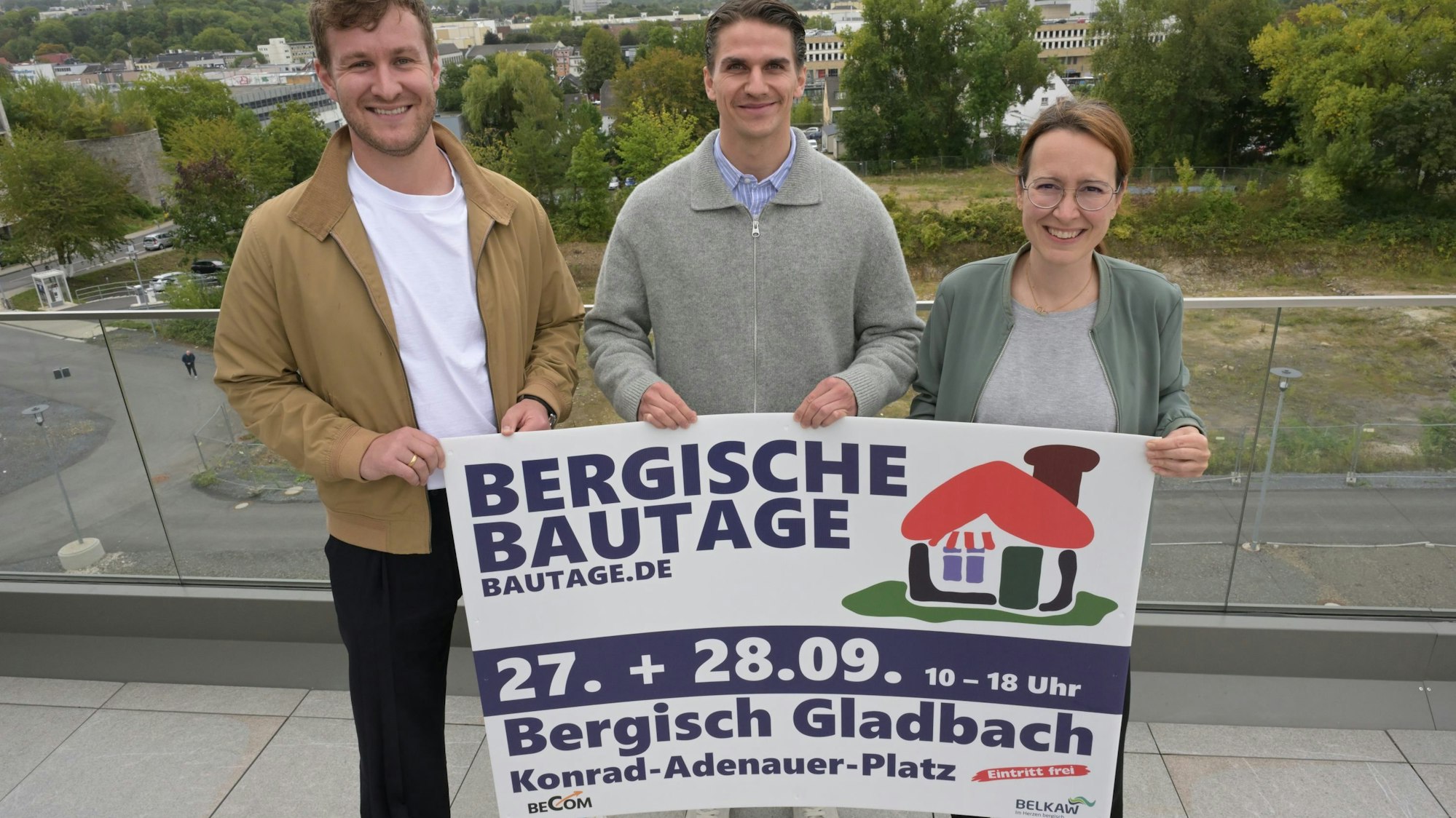 Drei Menschen halten auf einer Terrasse ein Plakat der Bergischen Bautage 2025.
