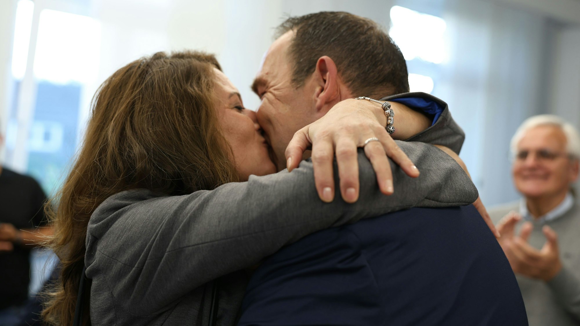 Die Eheleute küssen sich, während im Hintergrund die Besucher der Wahlparty applaudieren.