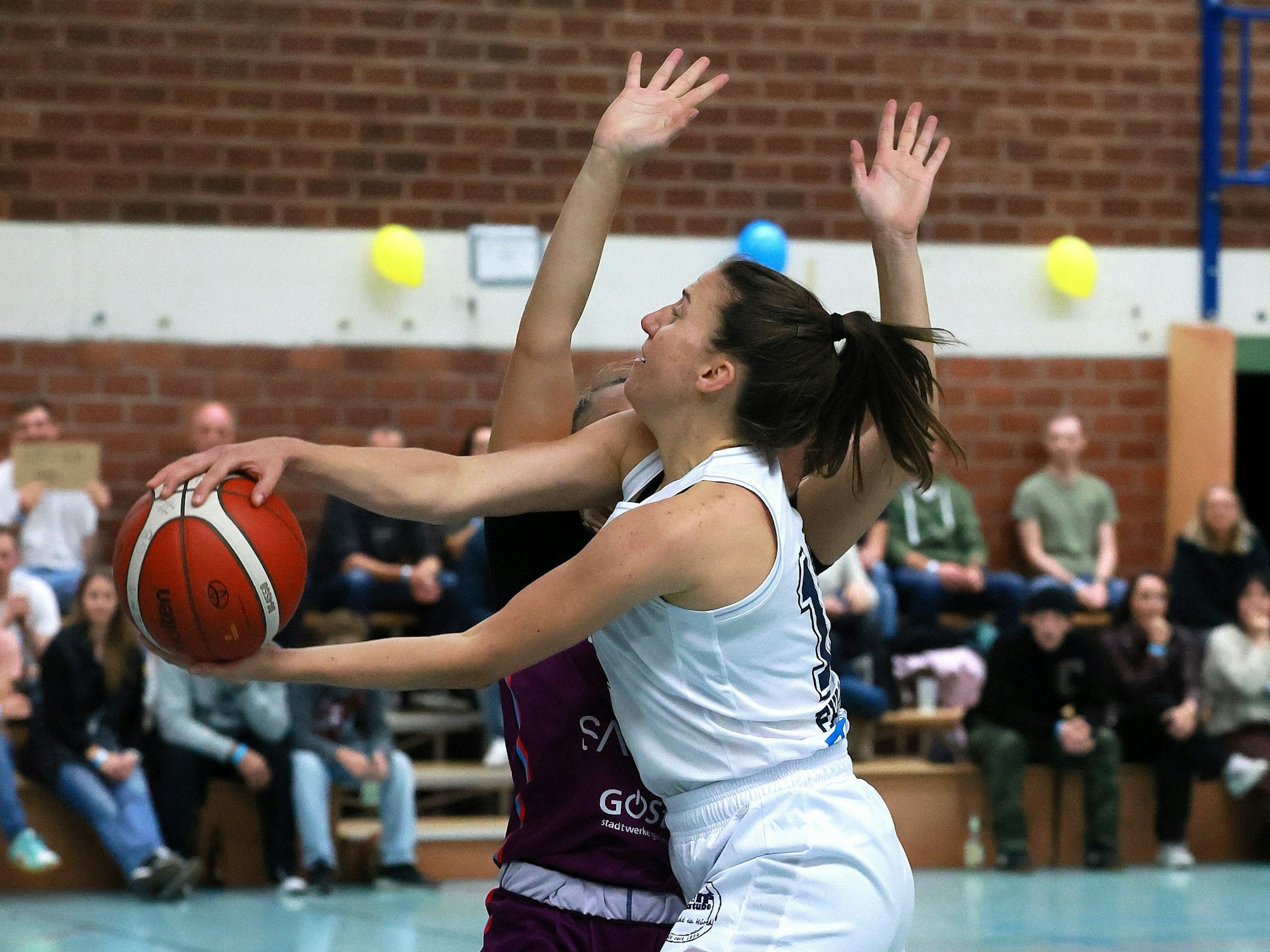 Das Bild zeigt eine Basketballerin, die mit dem Ball an ihrer Gegnerin in Richtung Korb zieht.