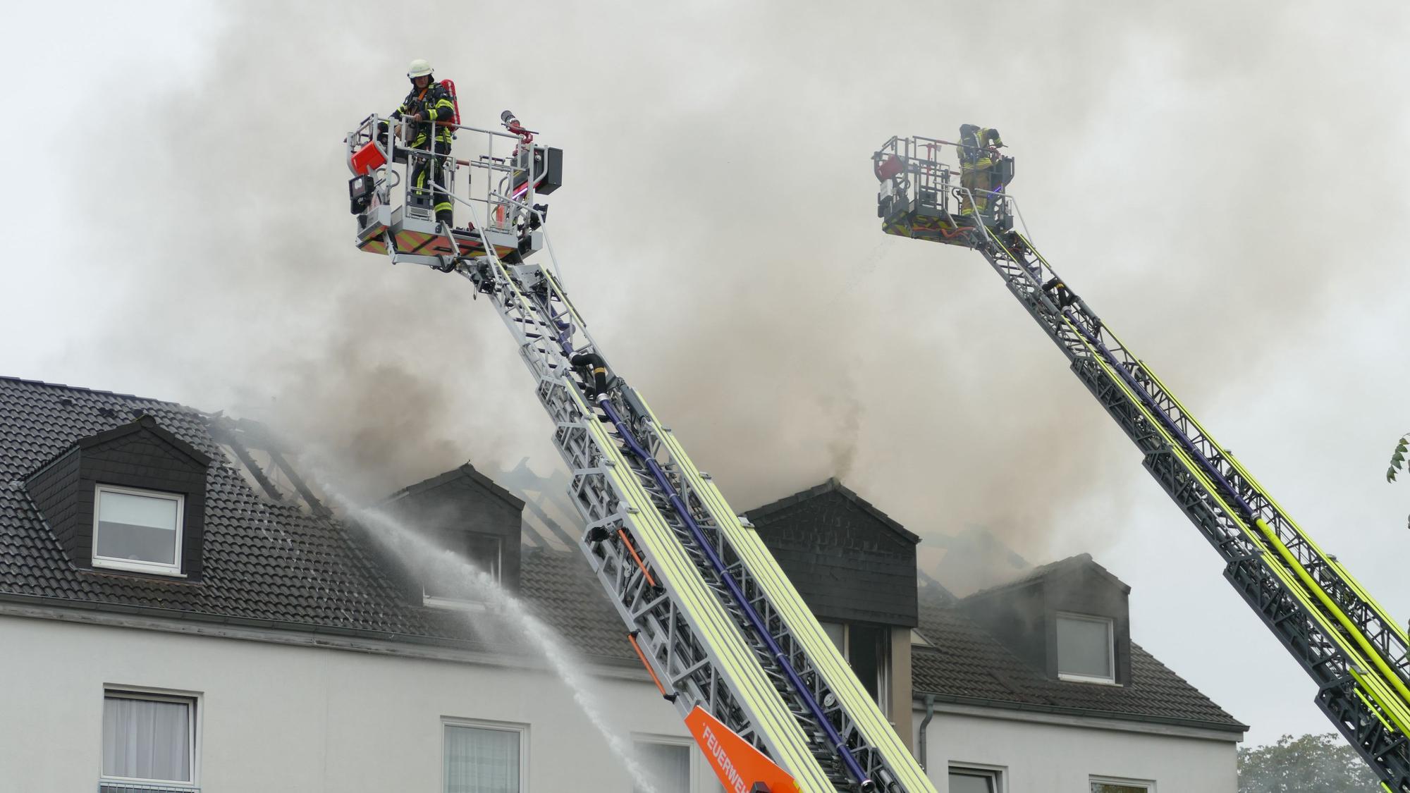 Feuerwehrleute stehen auf Drehleitern und löschen von oben.
