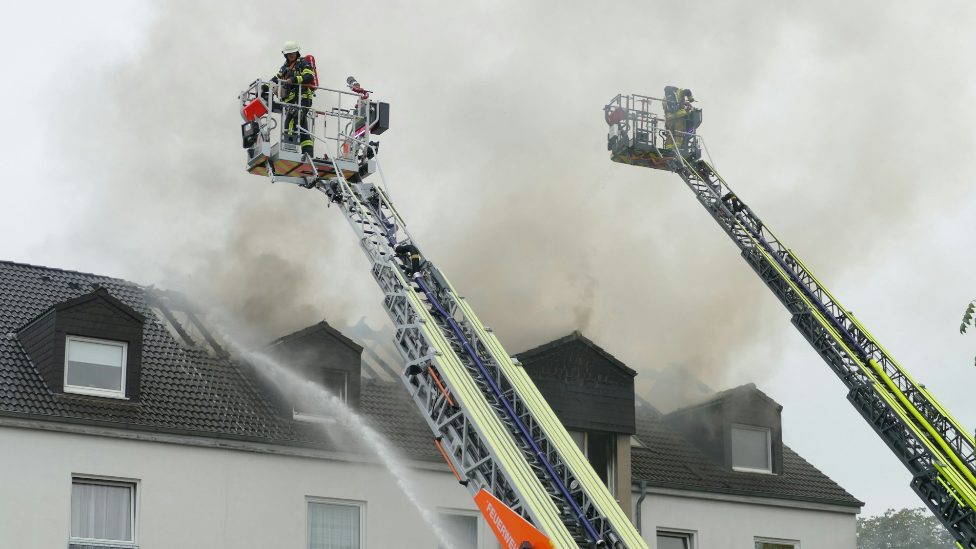 Feuerwehrleute stehen auf Drehleitern und löschen von oben.