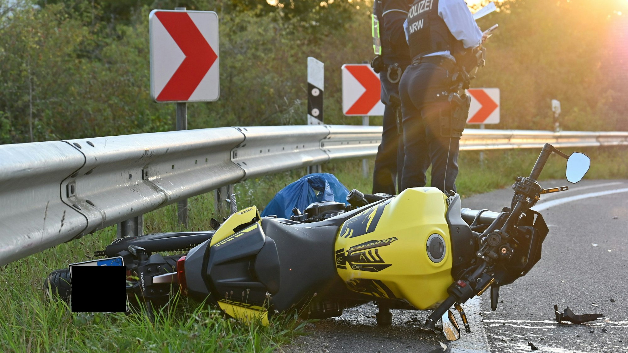 Das Bild zeigt ein Motorrad an einer Leitplanke und zwei Polizeibeamte.