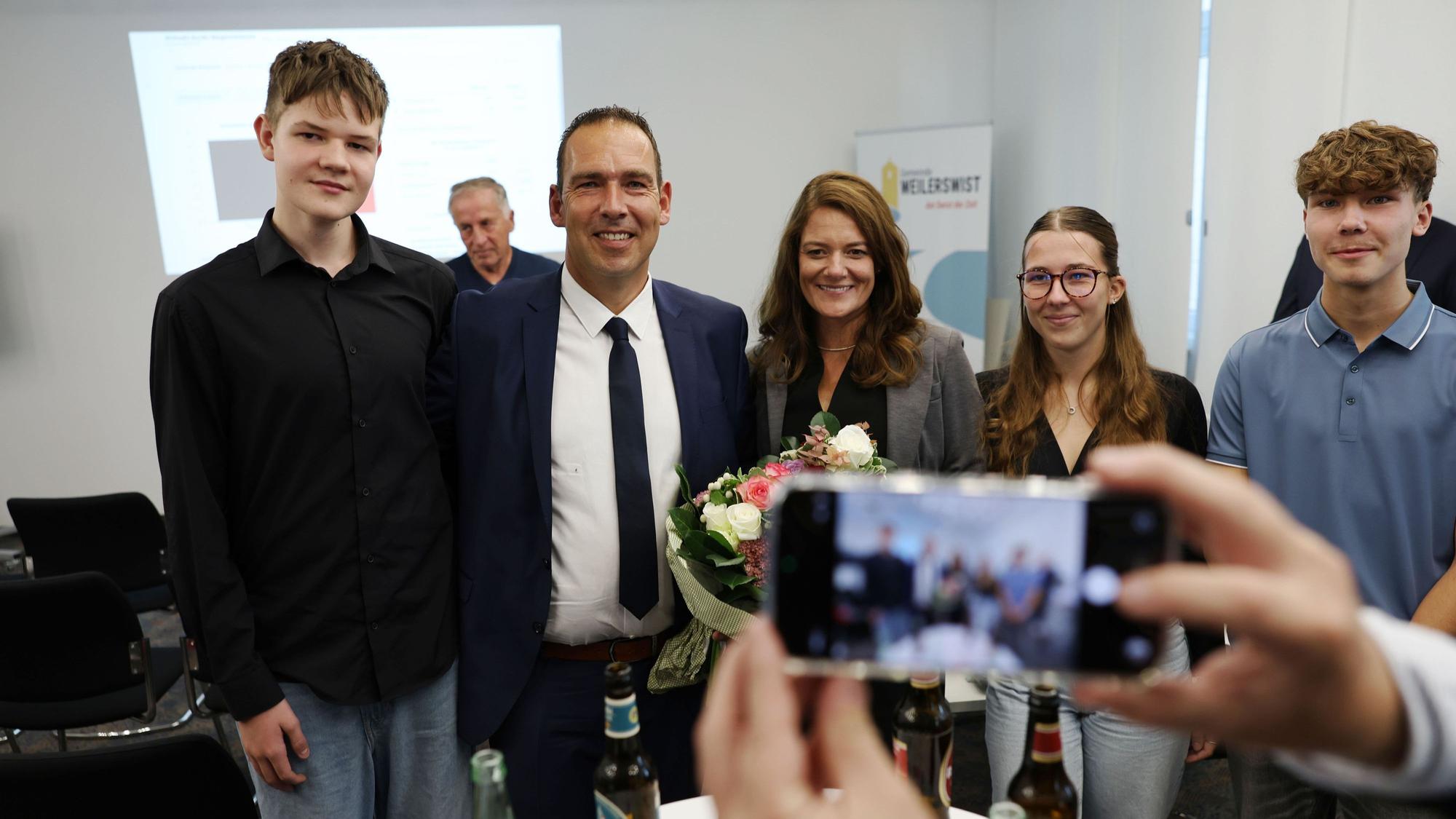 Der künftige Weilerswister Bürgermeister Dino Steuer steht mit seiner Frau Julia, Tochter Lara-Sophie und den beiden Söhnen Ben (l.) und Jan zusammen. Im Vordergrund ist ein Smartphone zu sehen, mit dem ein Foto der Familie gemacht wird