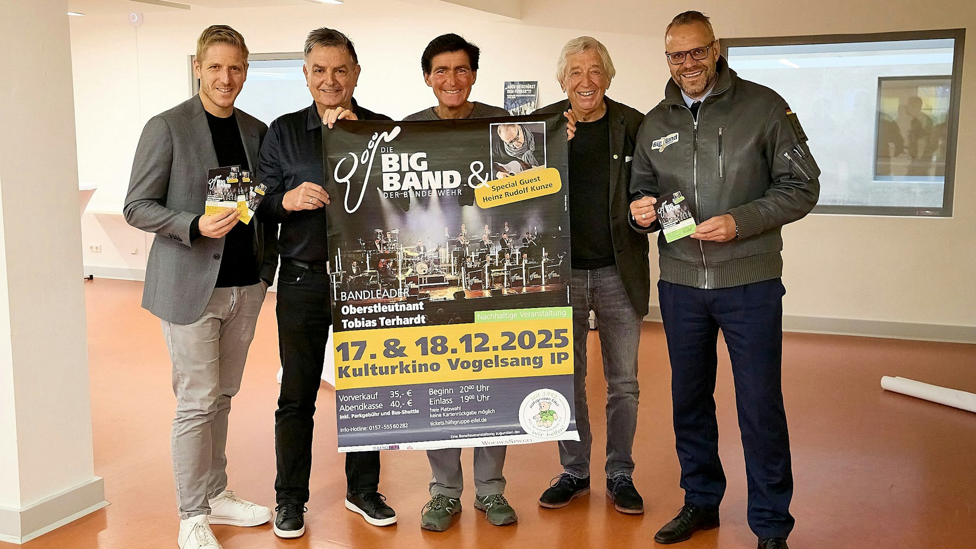 Markus Ramers (v.l.), Achim Liedtke, Thomas Kreyes, Willi Greuel und Johannes Langendorf stehen in einem Gang und halten ein Big Band Plakat in die Luft.