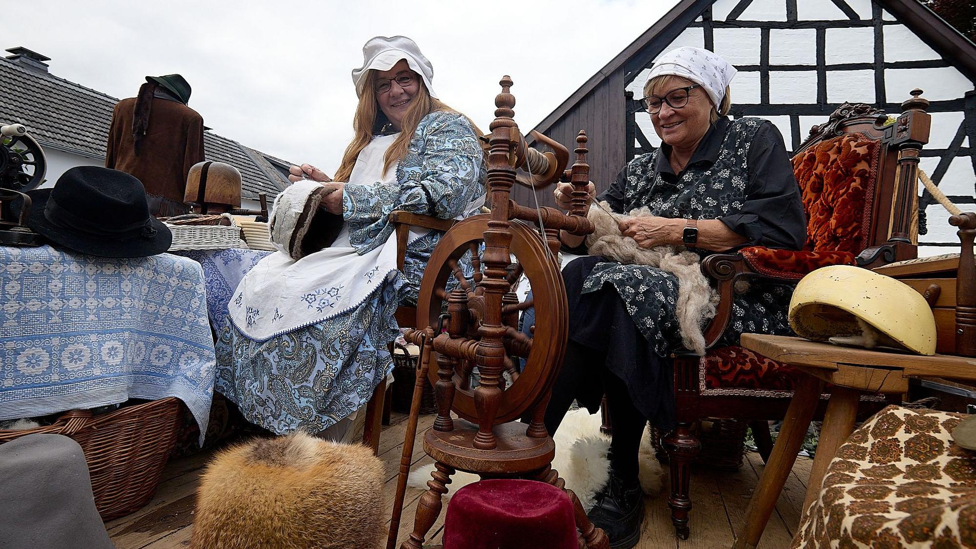 Das Bild zeigt eine Hutmacherin und eine Frau am Spinnrad in historischer Bekleidung.