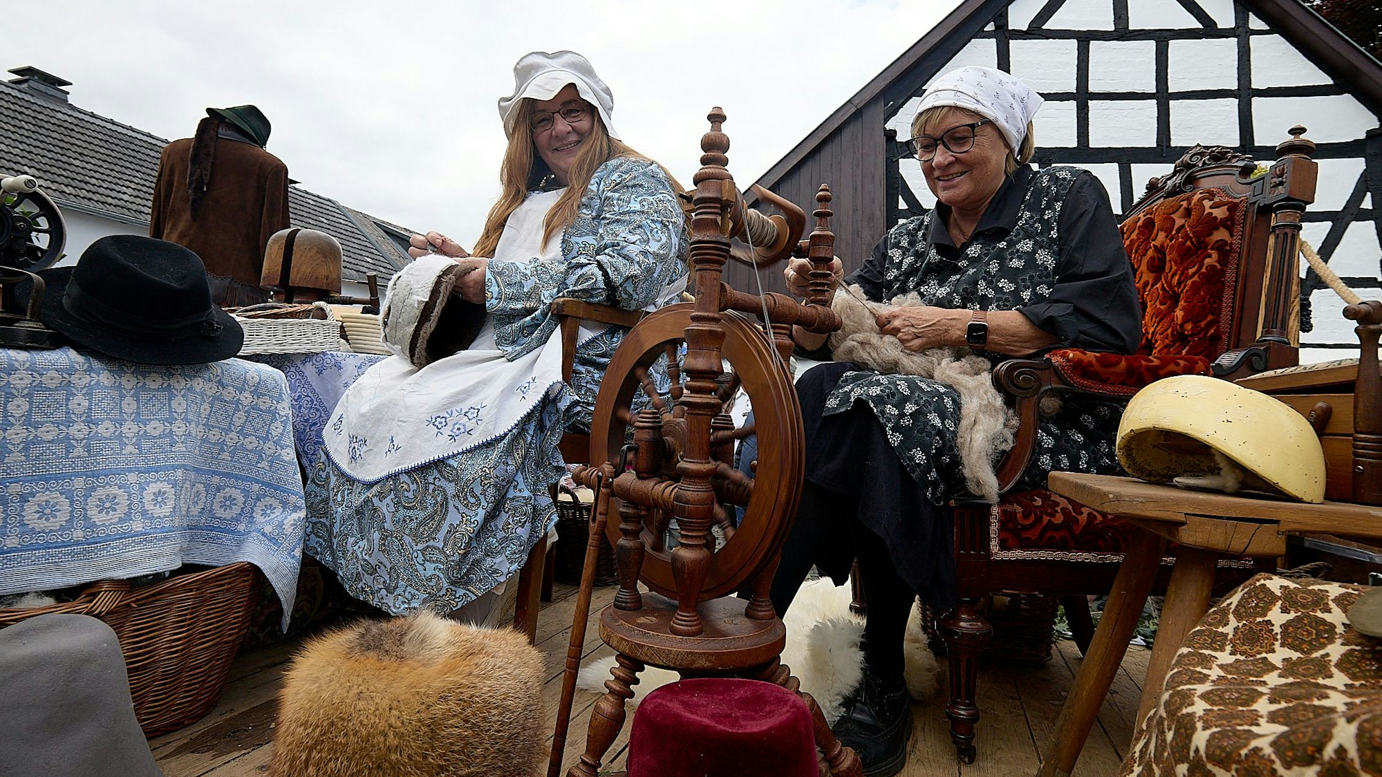 Das Bild zeigt eine Hutmacherin und eine Frau am Spinnrad in historischer Bekleidung.