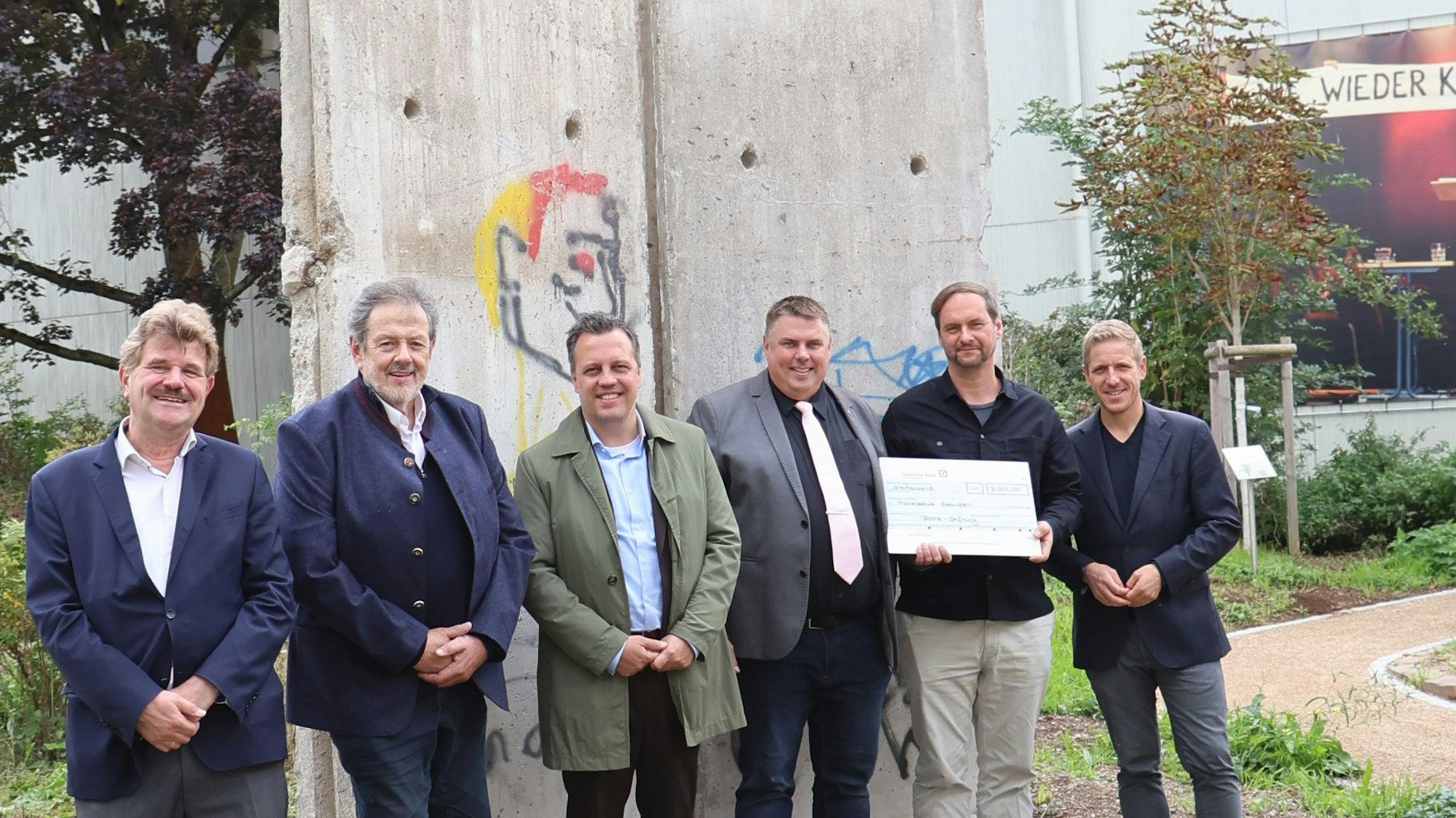 Politiker und der Schuldirektor der Marienschule Euskirchen Michael Mombaur stehen vor Originalelementen der Berliner Mauer.