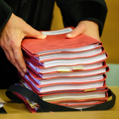 Ein Staatsanwalt legt einen Stapel Akten vor Prozessbeginn auf seinen Tisch im Gericht.