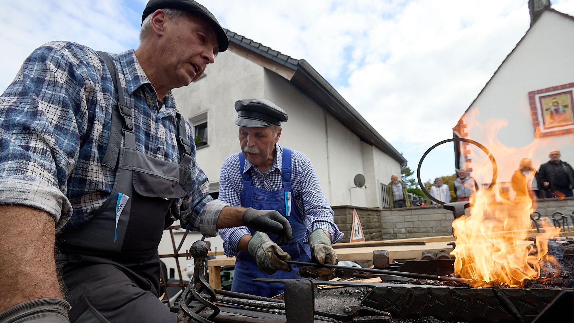 Zwei Männer sitzen auf einem Wagen im Erntedankzug an einem Schmiedefeuer. Sie stellen Nägel her.