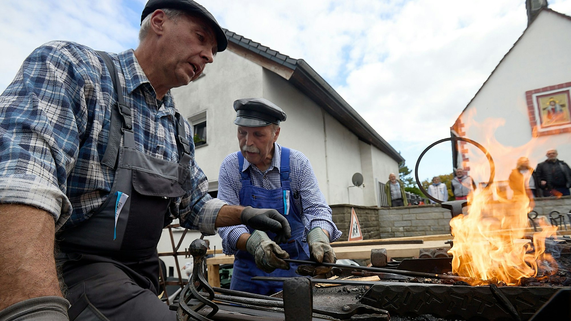 Zwei Männer sitzen auf einem Wagen im Erntedankzug an einem Schmiedefeuer. Sie stellen Nägel her.