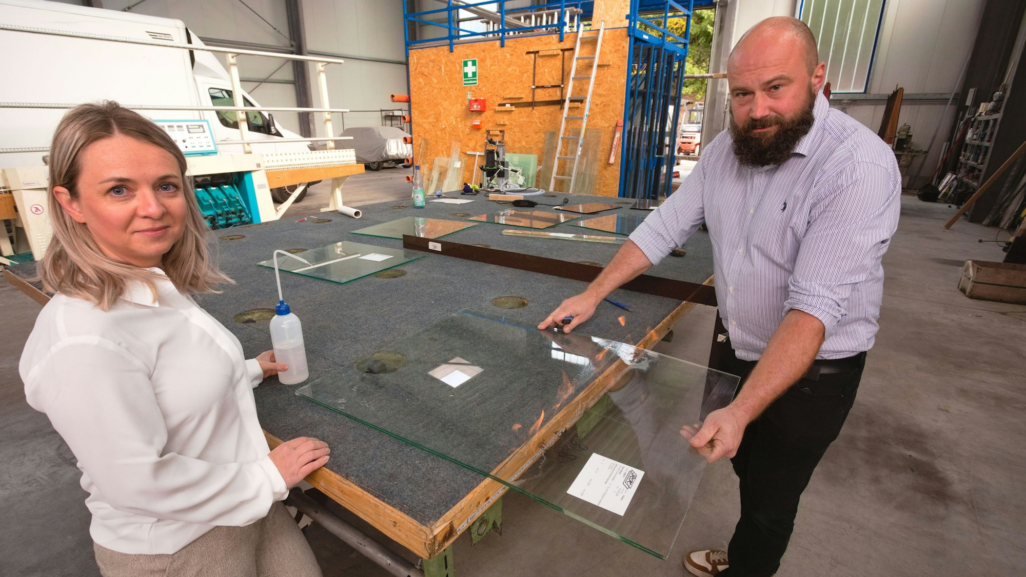 Eine Frau und ein Mann demonstrieren die Arbeit mit einer Glasscheibe in ihrer Werkstatt.