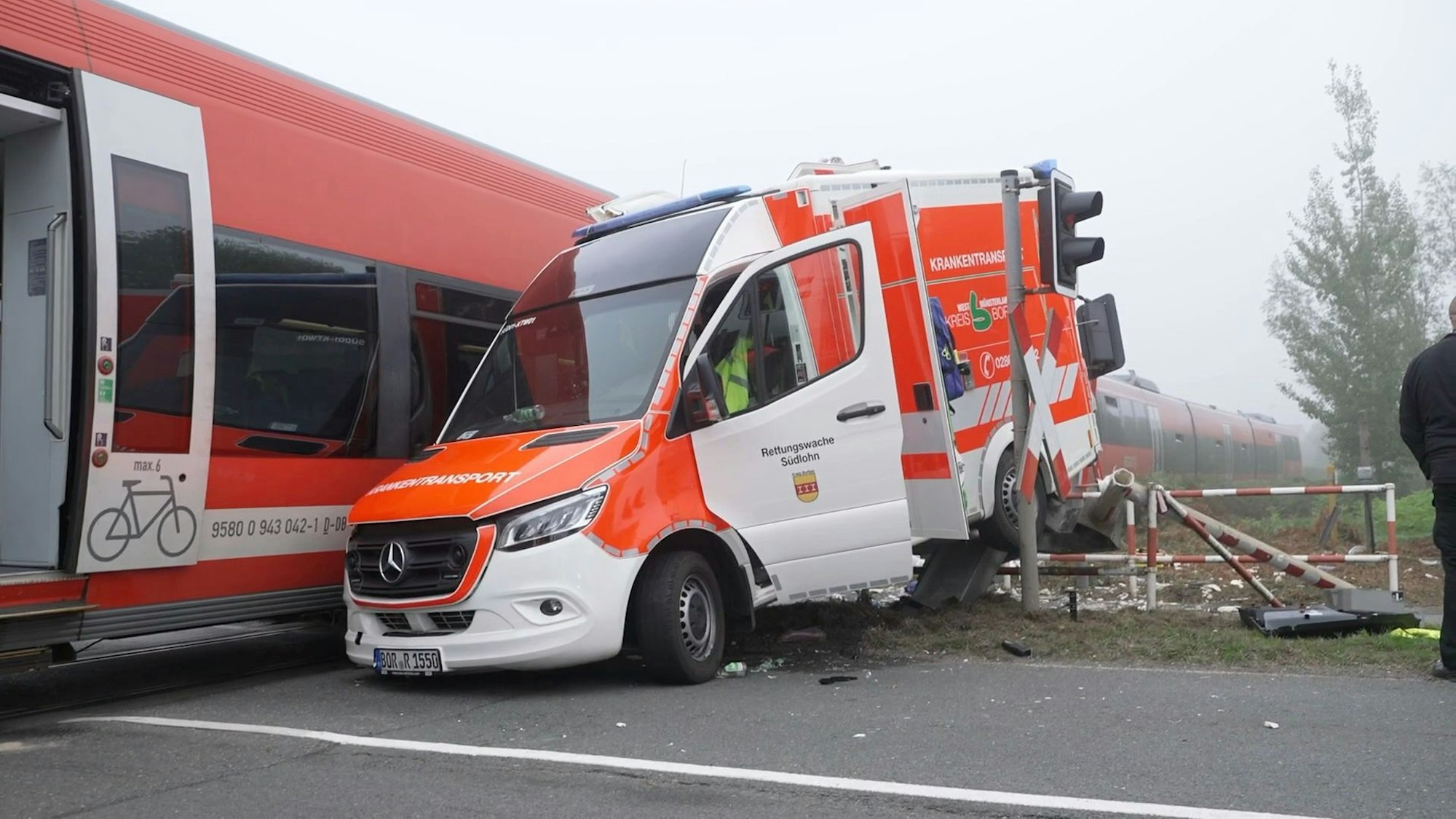 Ein Rettungswagen steht neben einem Regionalzug. Der Wagen ist an einem Bahnübergang mit dem Zug kollidiert.