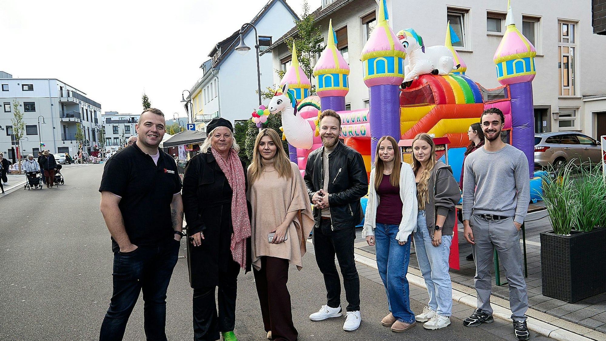 Eine Gruppe Männer und Frauen steht auf der Bahnhofstraße in Kall, im Hintergrund ist eine bunte Hüpfburg für Kinder zu sehen.