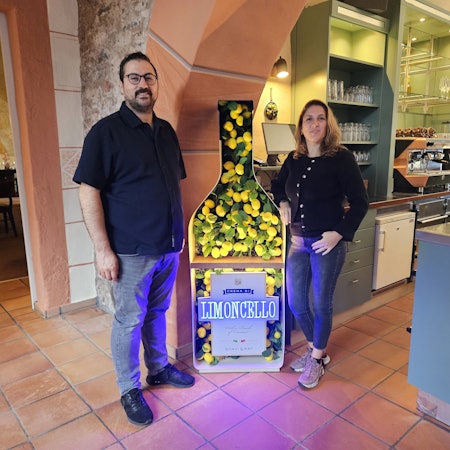 Melih Aydogdu und seine Frau Özgül stehen neben einer großen Werbung für Limoncello.