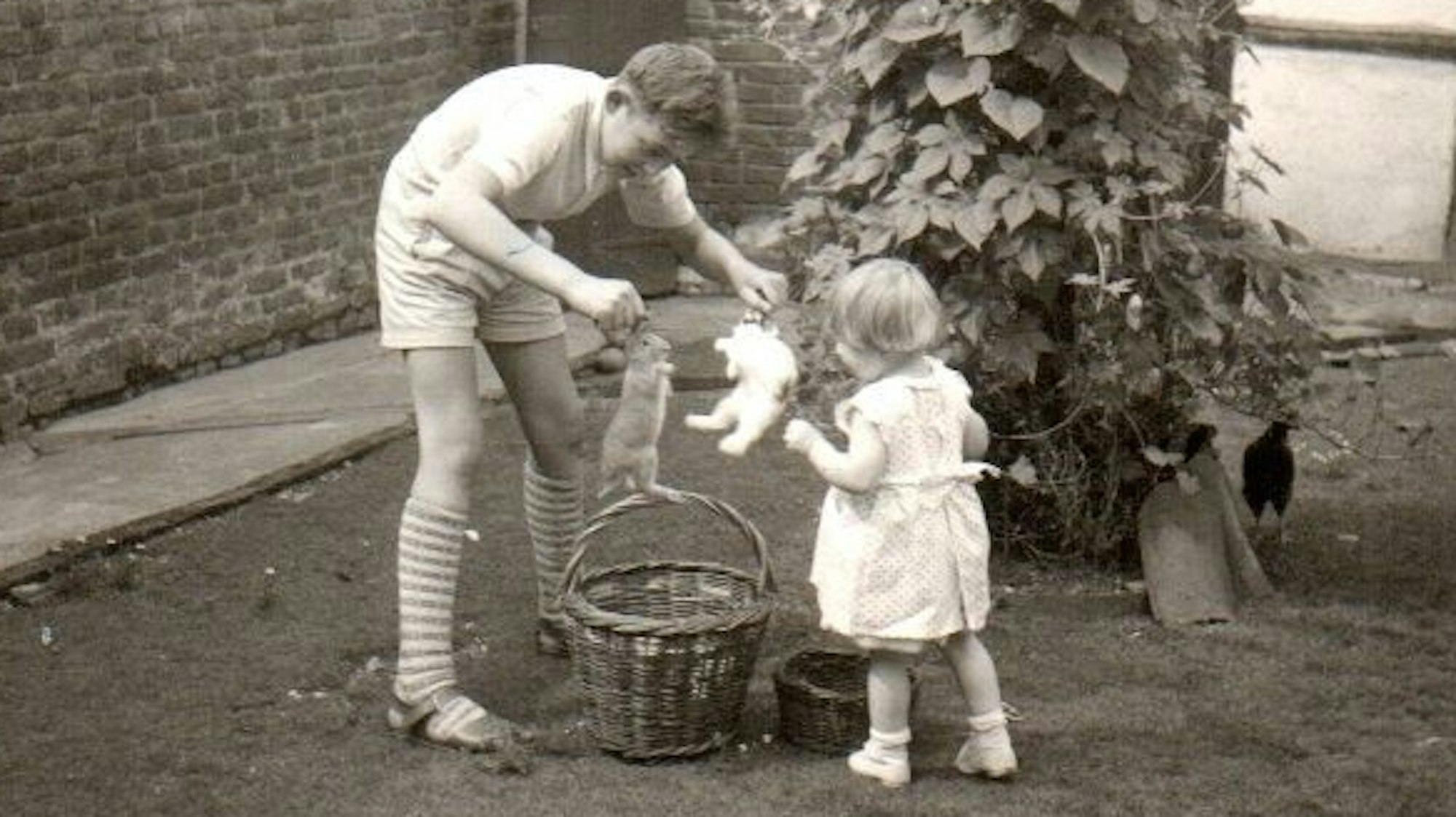 Das Schwarz-Weiß-Foto zeigt einen Jugendlichen, der zwei Kaninchen trägt, und ein Mädchen.