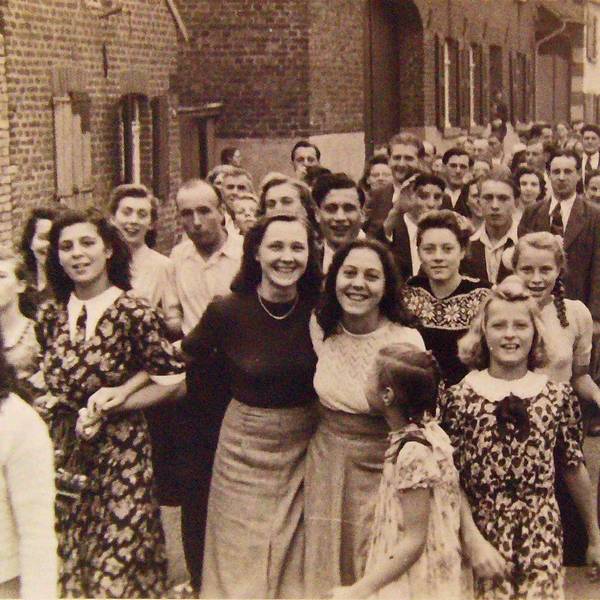 Zu sehen sind viele Menschen auf einer Dorfstraße auf einem Schwarz-Weiß-Foto.