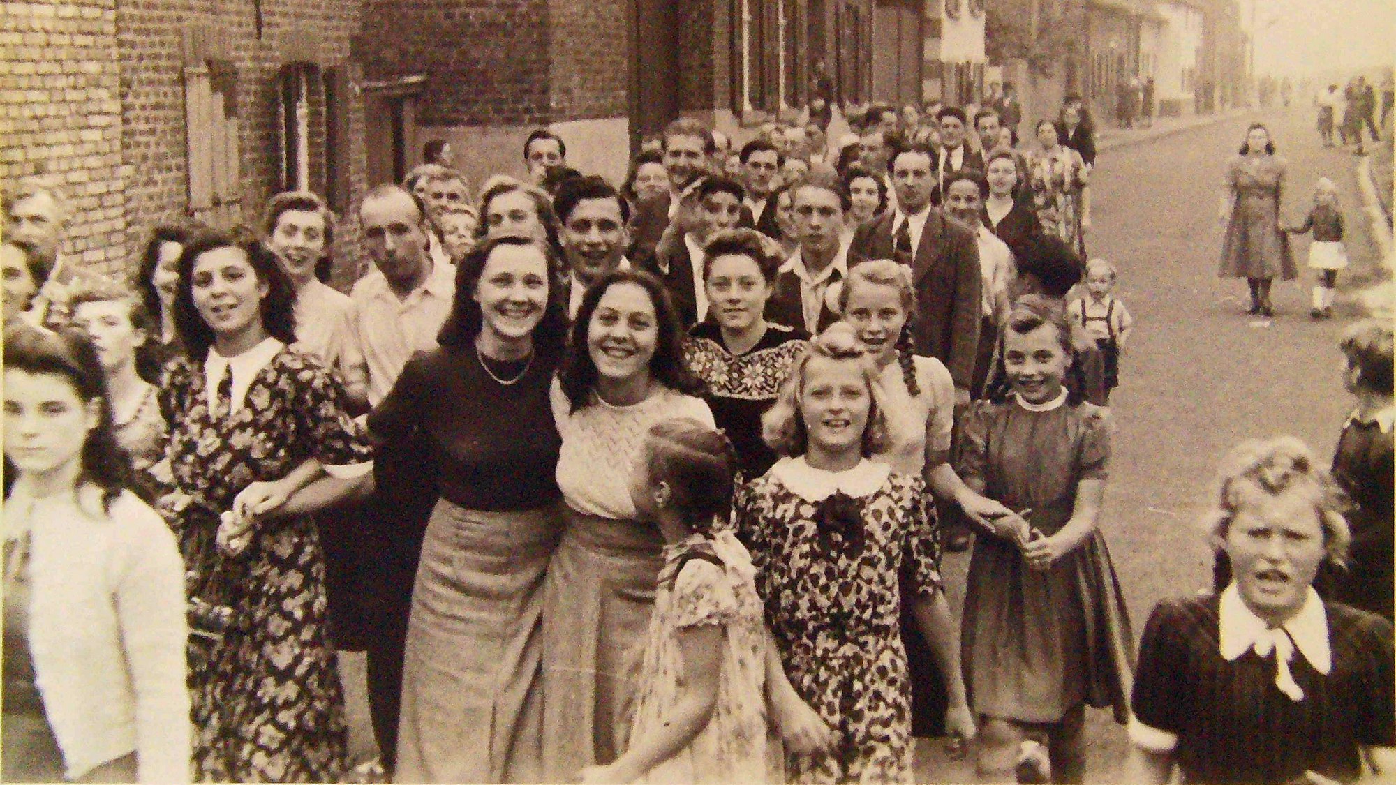 Zu sehen sind viele Menschen auf einer Dorfstraße auf einem Schwarz-Weiß-Foto.