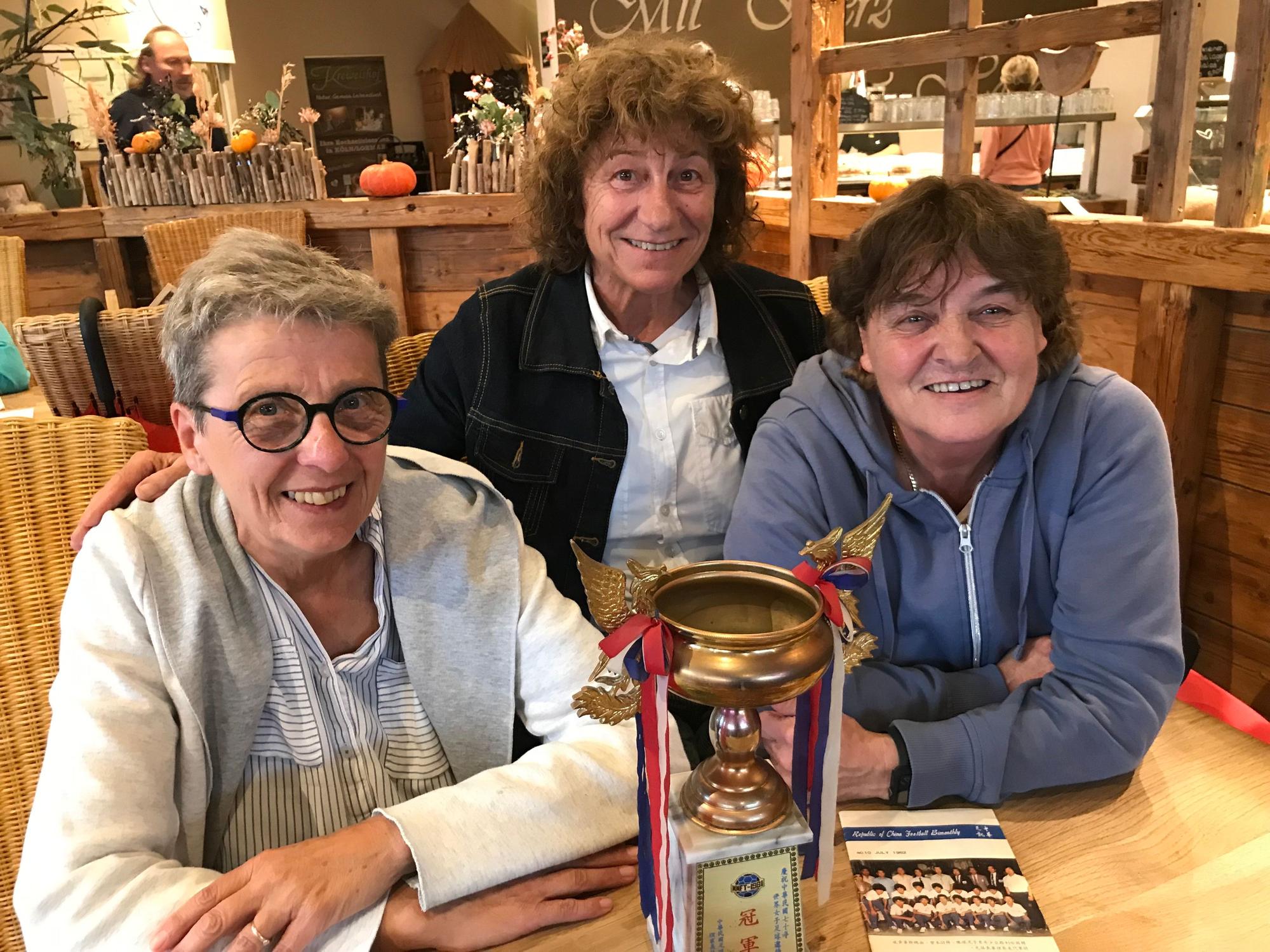 Pokal, Turnierheft und drei Weltmeisterinnen vom Team der SSG 09 Bergisch Gladbach (v.l.: Hannelore Geilen, Monika Steinmetz und Hildegard Frauenrath), die 1981 bei der inoffiziellen Frauenfußball-WM in Taipeh den Titel holten.