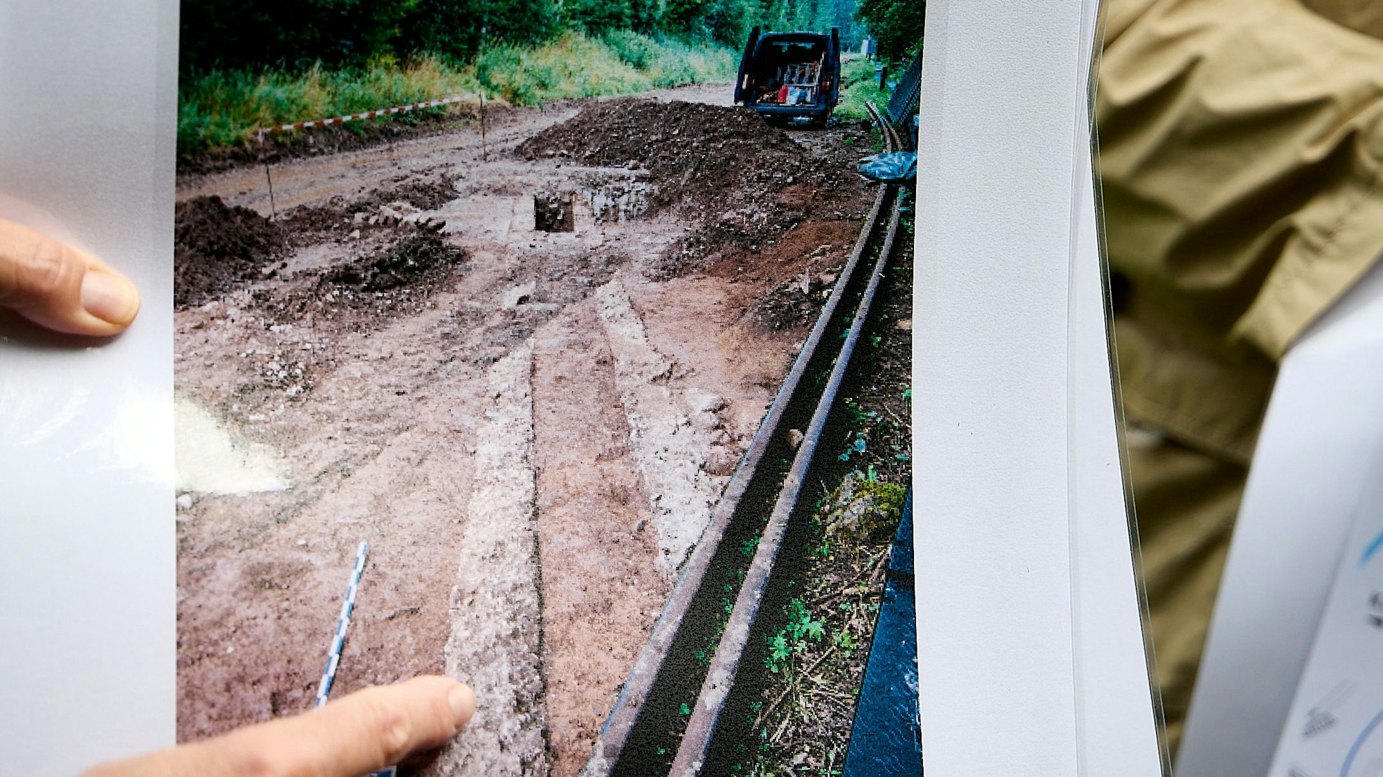 Auf einer Fotografie sind Spuren des Römerkanals festgehalten. Ein Finger zeigt hierauf.