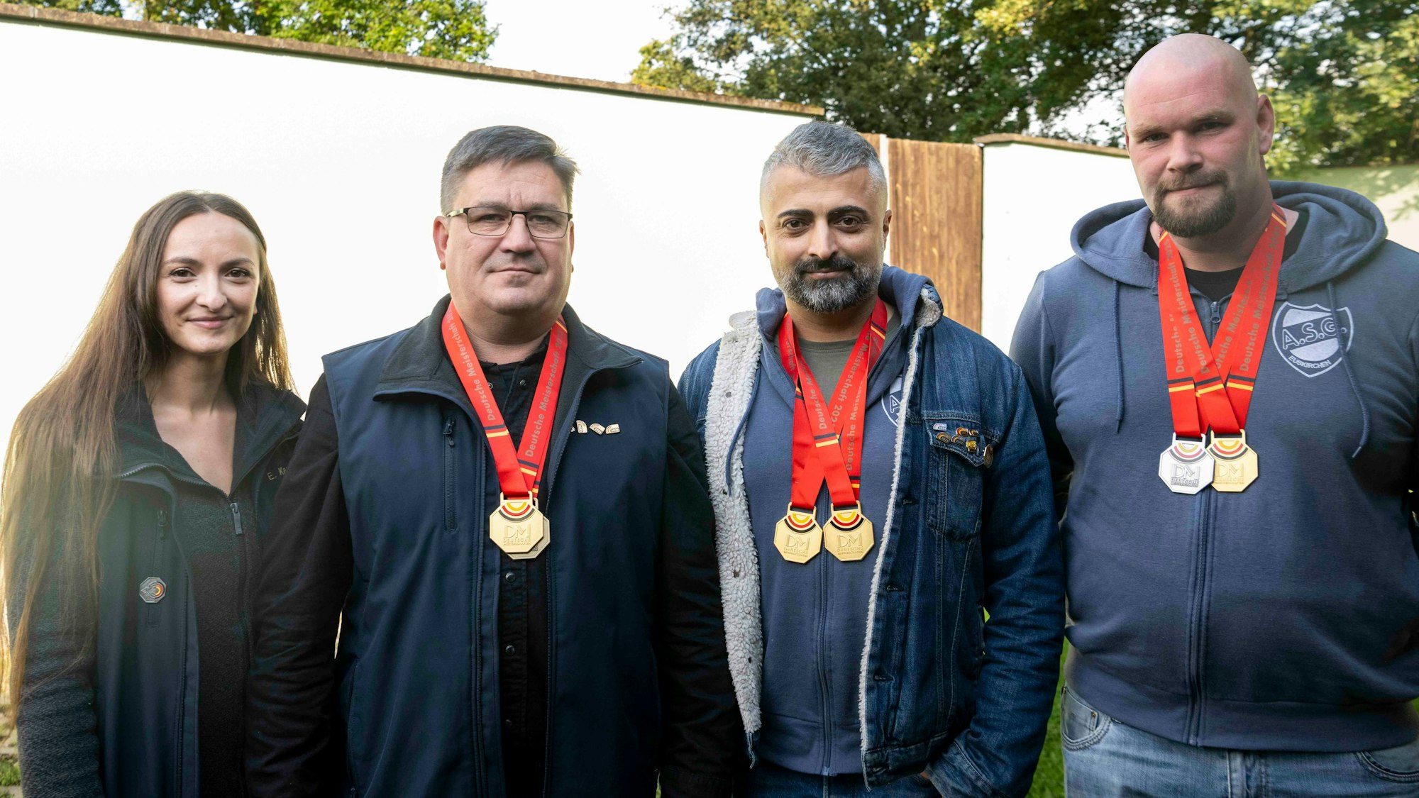 Drei Männer und eine Frau stehen nebeneinander. Die Männer tragen Medaillen um den Hals, die sie im Schießen gewonnen haben.