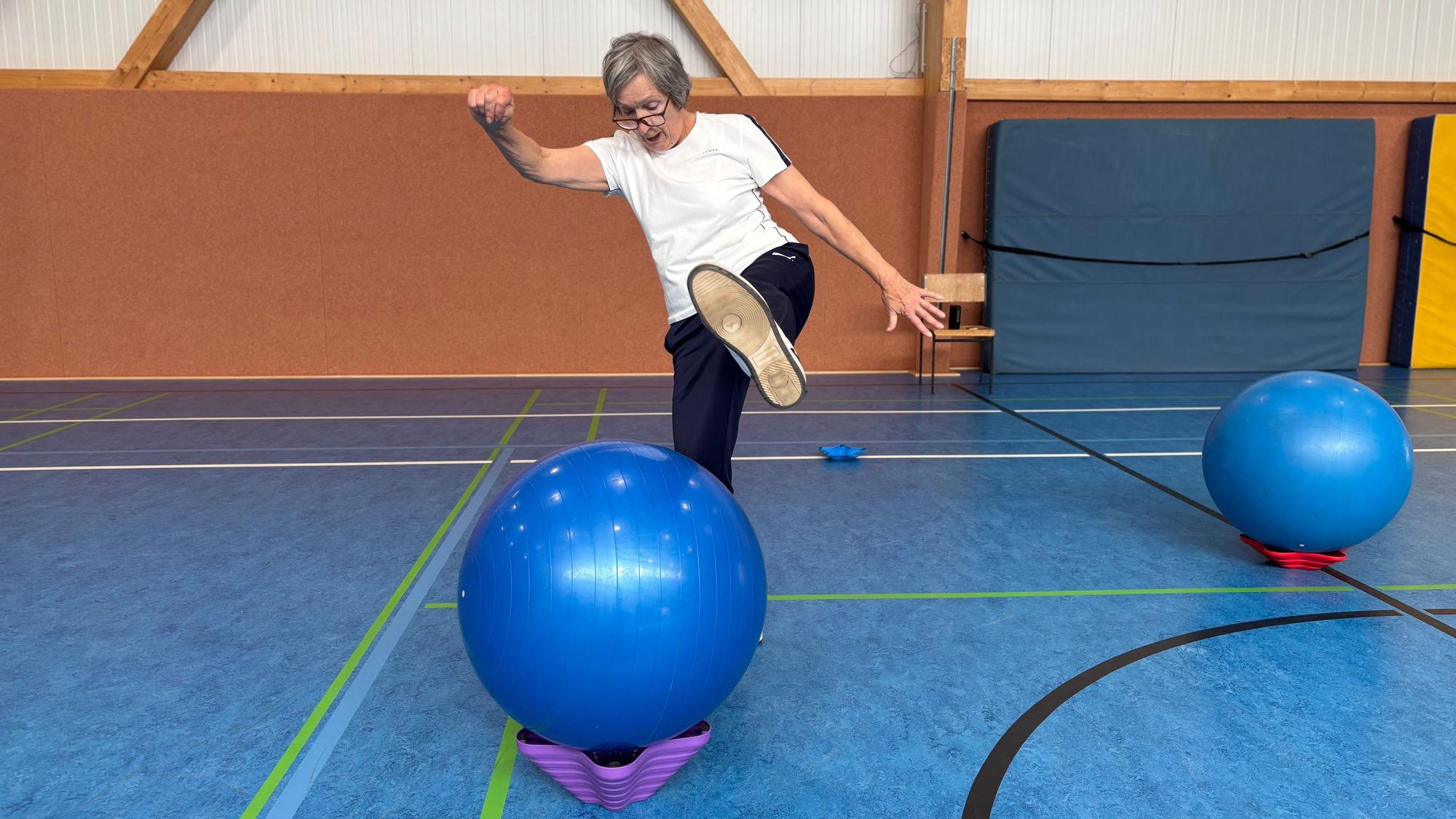 Eine ältere Frau in sportlicher Kleidung tritt über einen Gymnastikball.