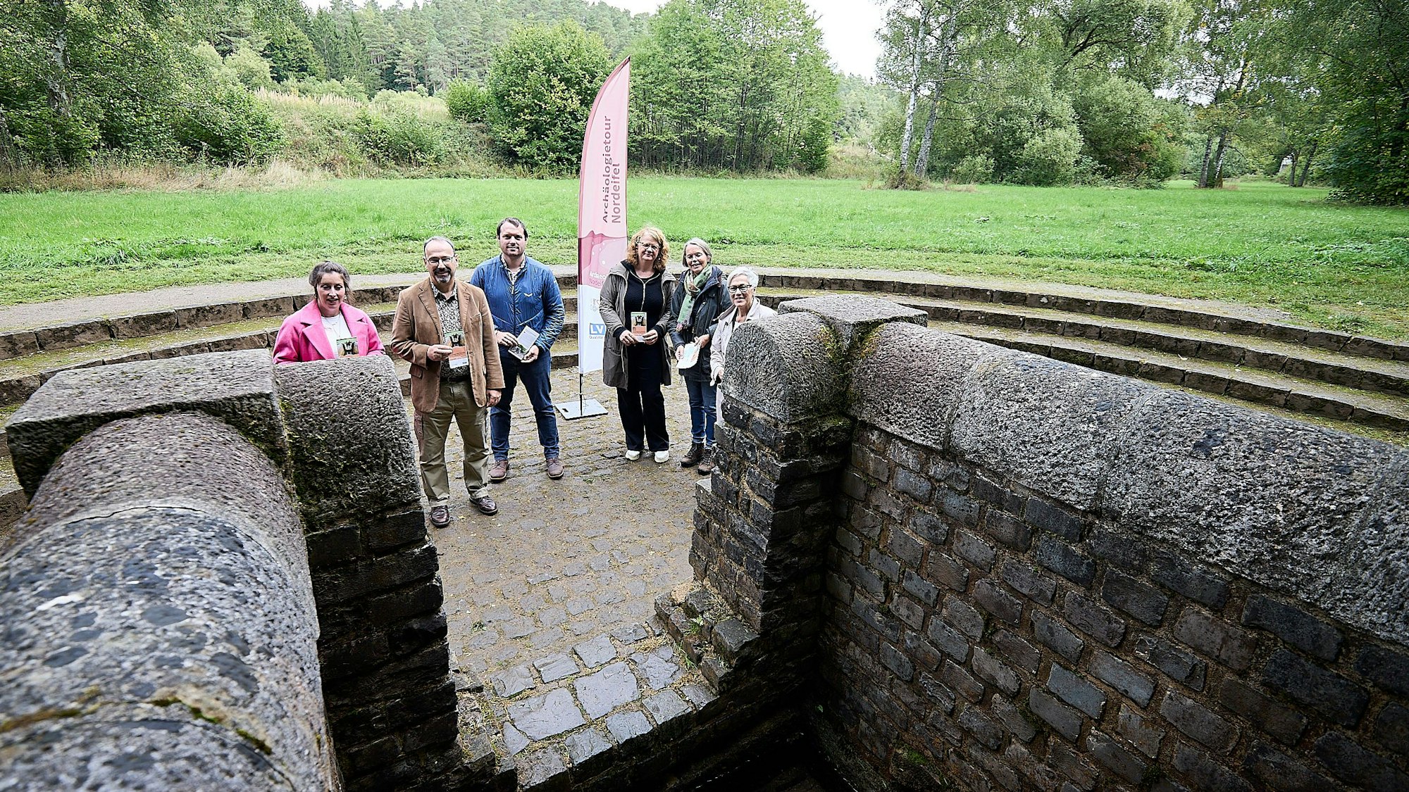 Sechs Menschen stehen beim Grünen Pütz in Nettersheim. Im Hintergrund stehen Bäume.