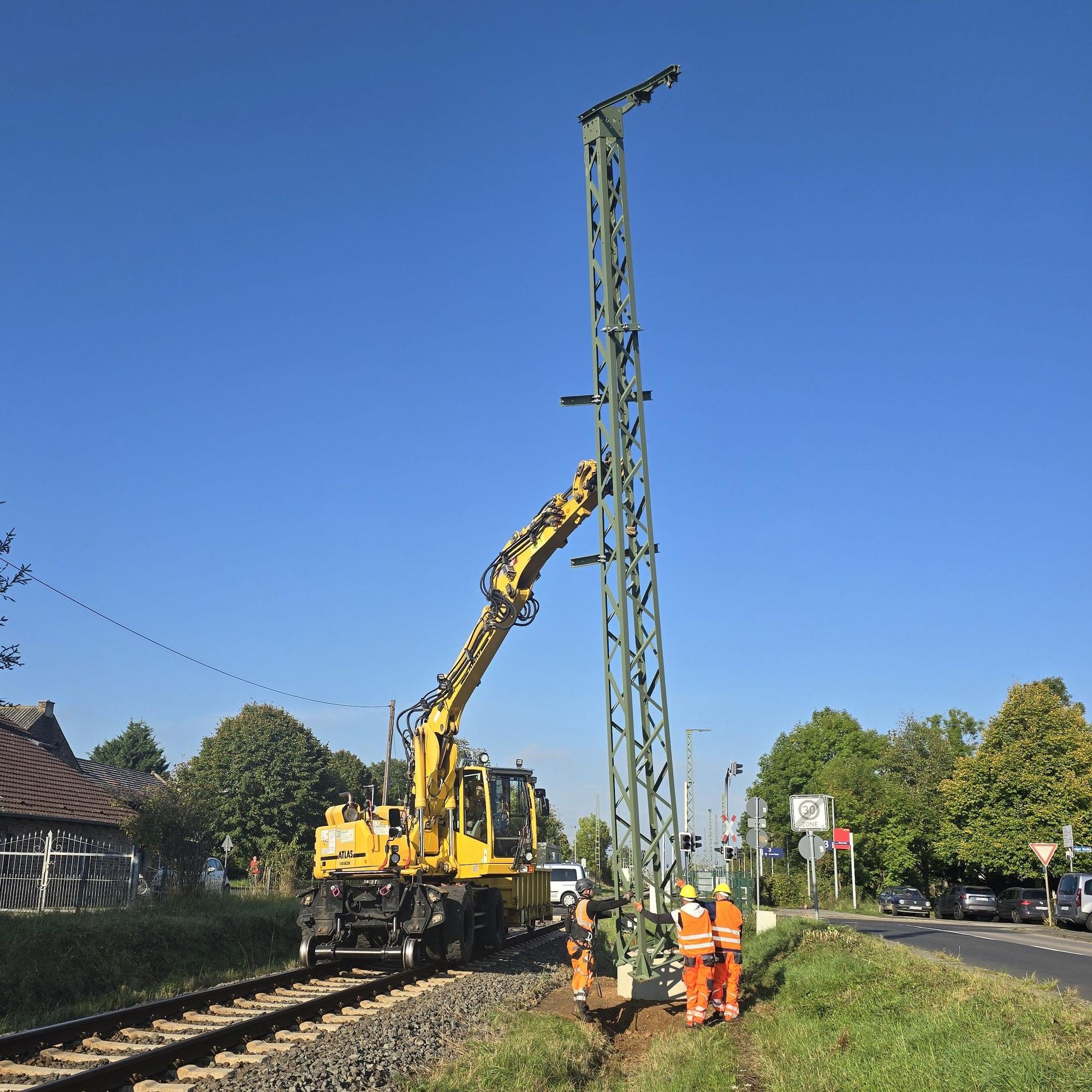 Bahnarbeiter montieren den Mast der Oberleitung, der von einem Kran aufgerichtet worden ist.